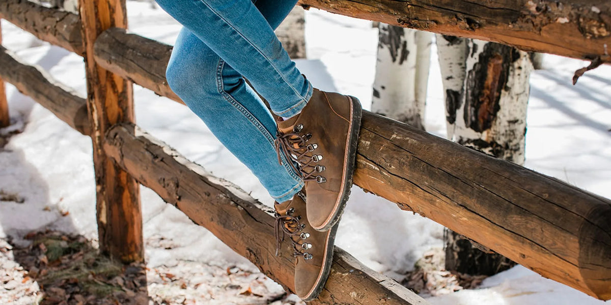 Brown leather lace-up boots worn with blue jeans beside a rustic snowy fence