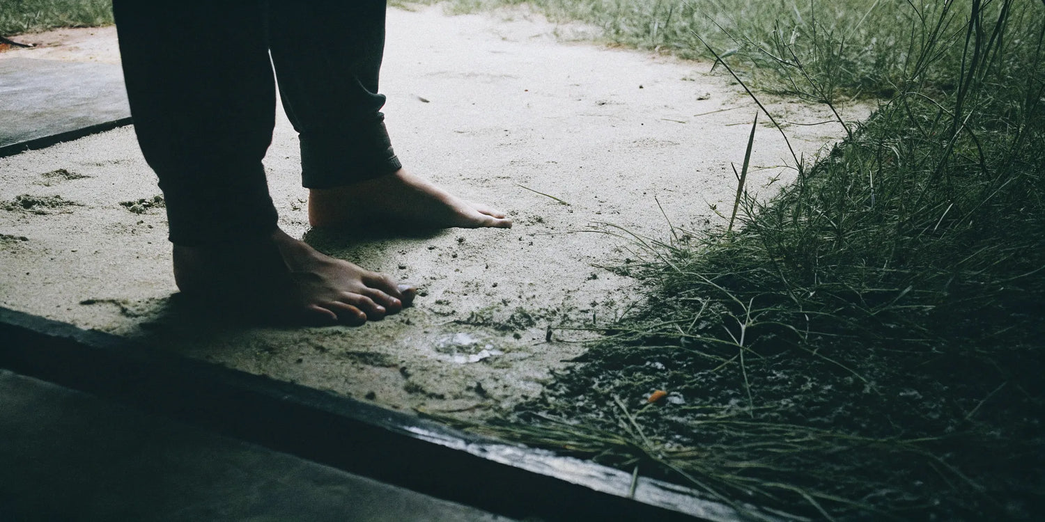 A close-up of feet on grass, sand, and concrete surfaces for grounding.