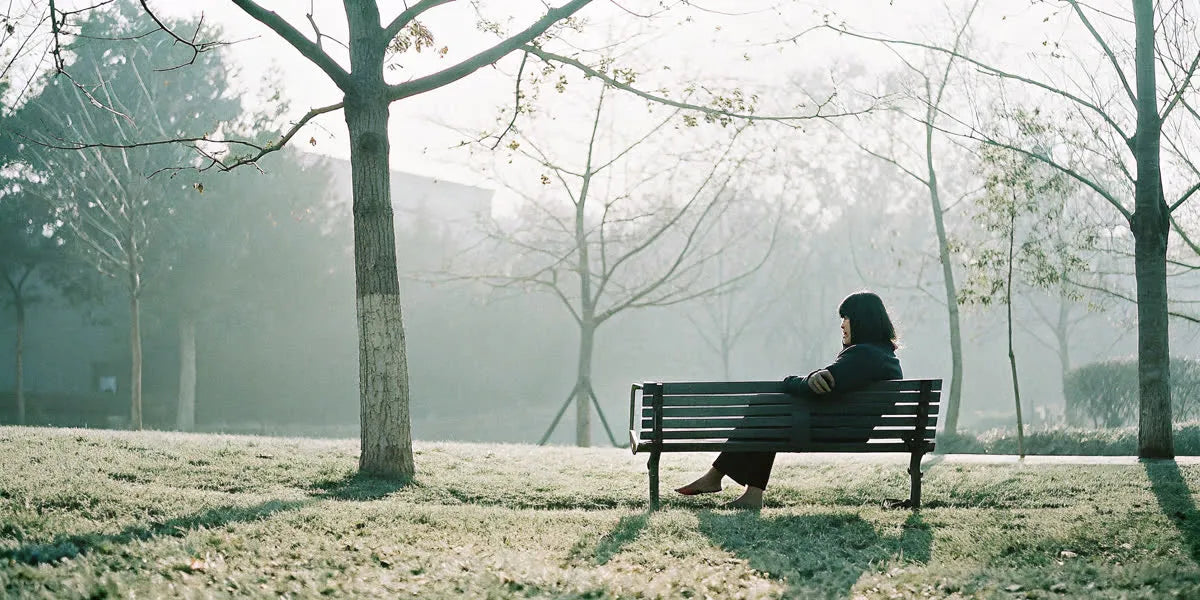 Woman sitting on a park bench grounding her bare feet on grass in soft sunlight