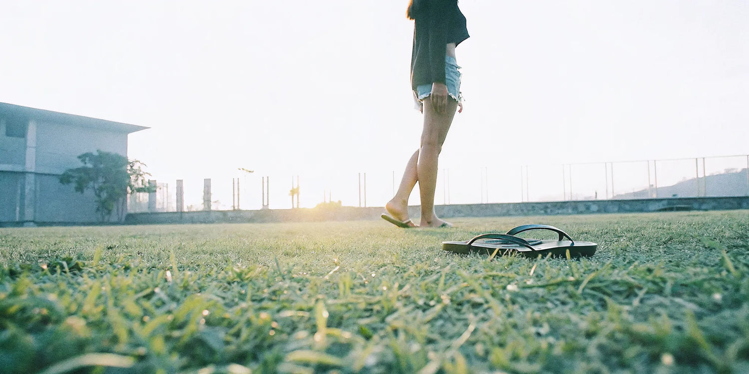 Grounding sandals and flip flops on grass beside bare feet