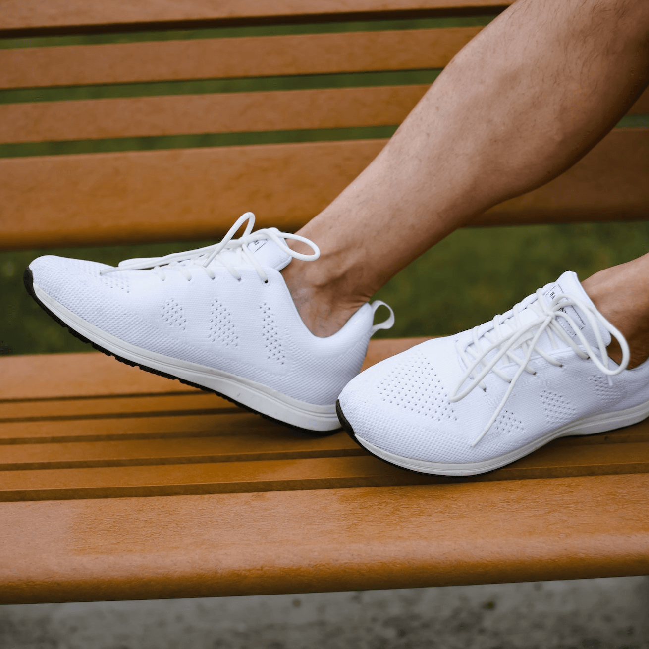 Man wearing white grounding lace-up sneakers on wooden bench