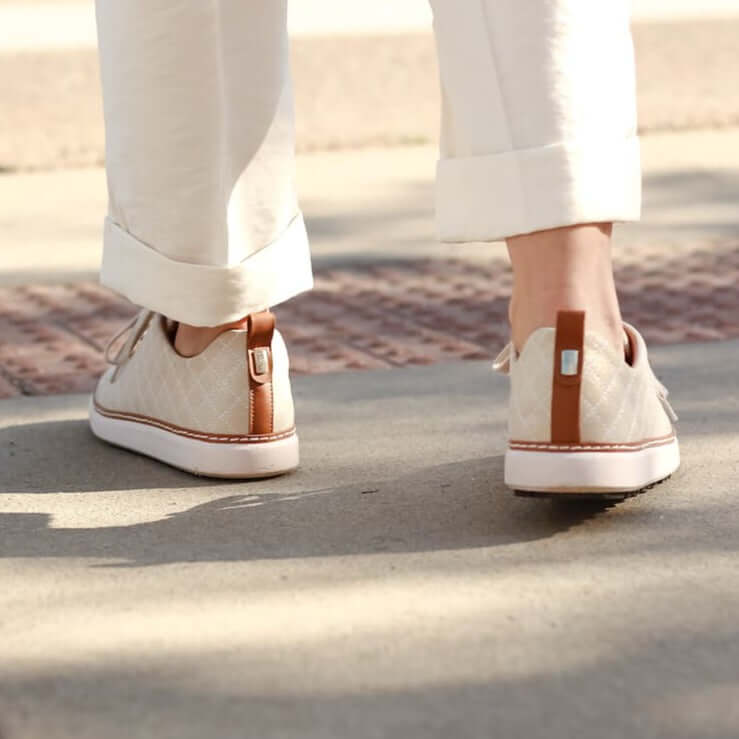 Woman walking away showing cognac accents on heel of gold creme quilted grounding walker