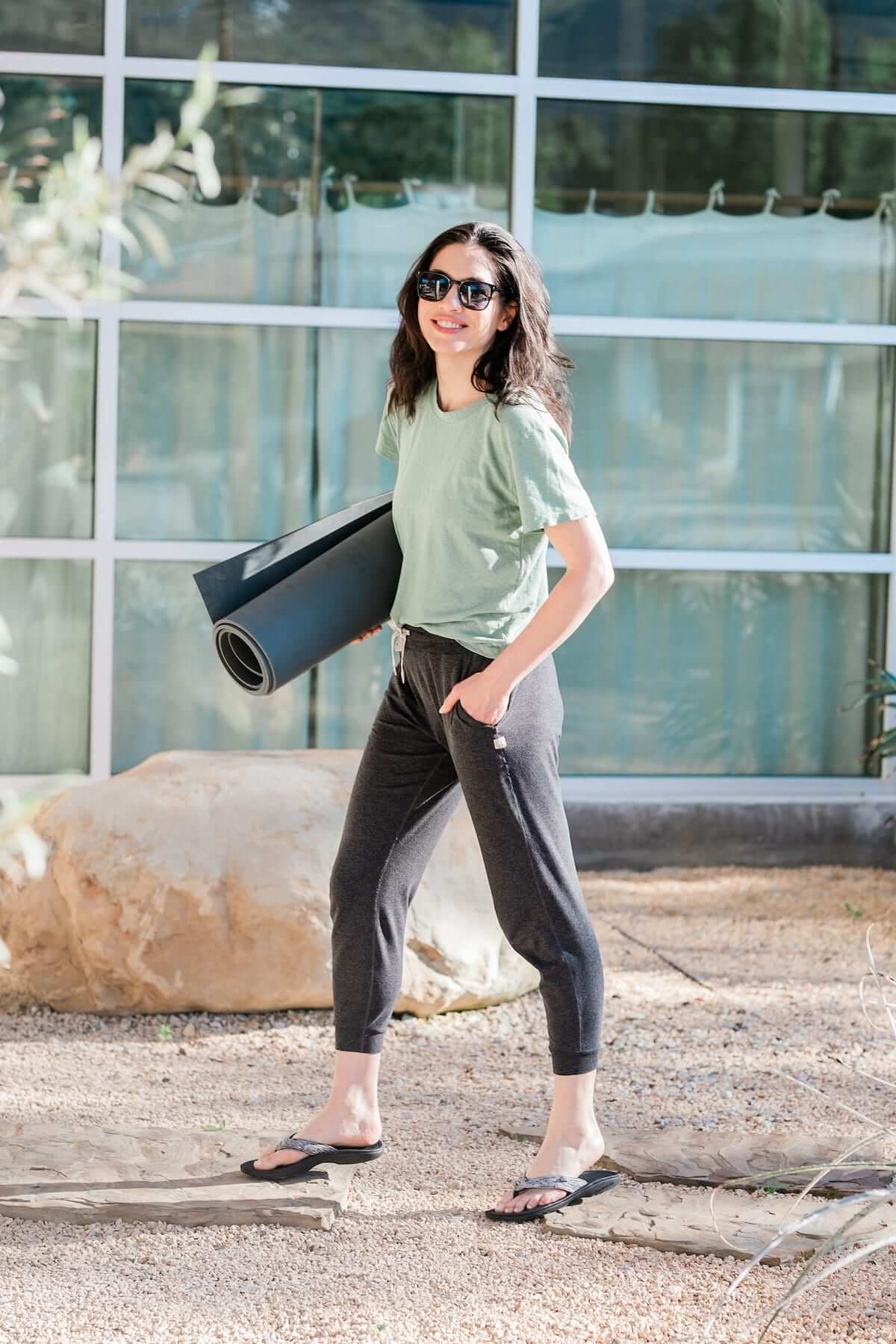 Woman with yoga mat walking on stone and gravel wearing Harmony 783 heather grey sandal conductive
footbed earthing flip flops