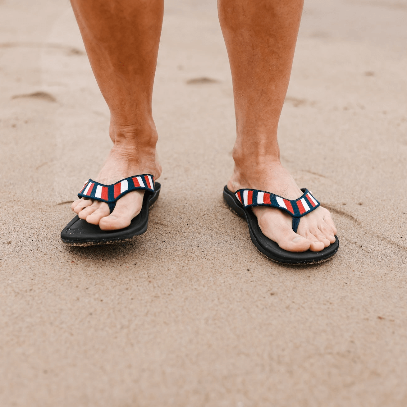 Close up of man standing on sand at the beach wearing Harmony 783 red white and blue striped knit conductive
footbed earthing