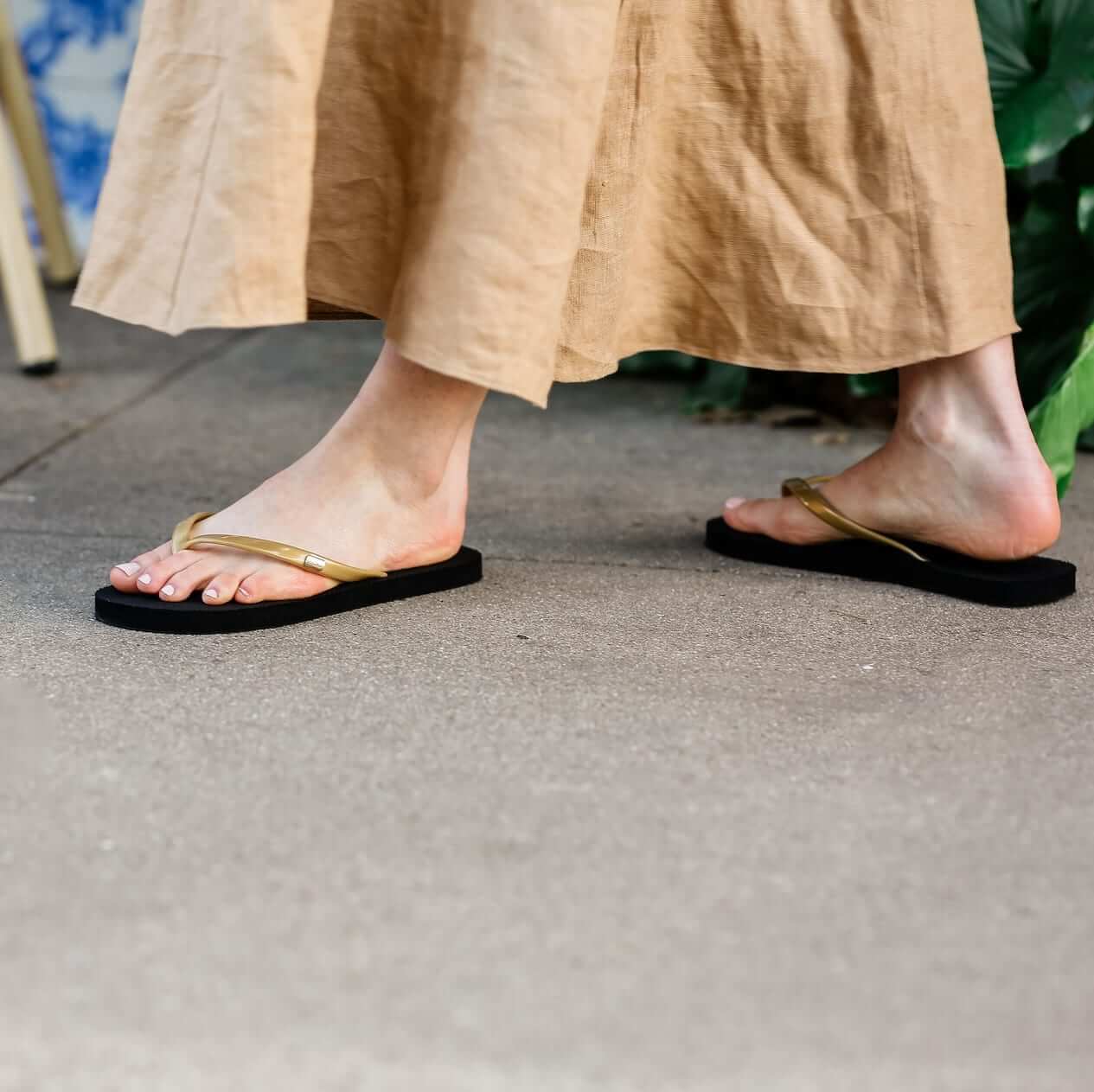 Close up of woman standing sidewalk wearing Harmony 783 black and gold fully conductive footbed earthing flip flops