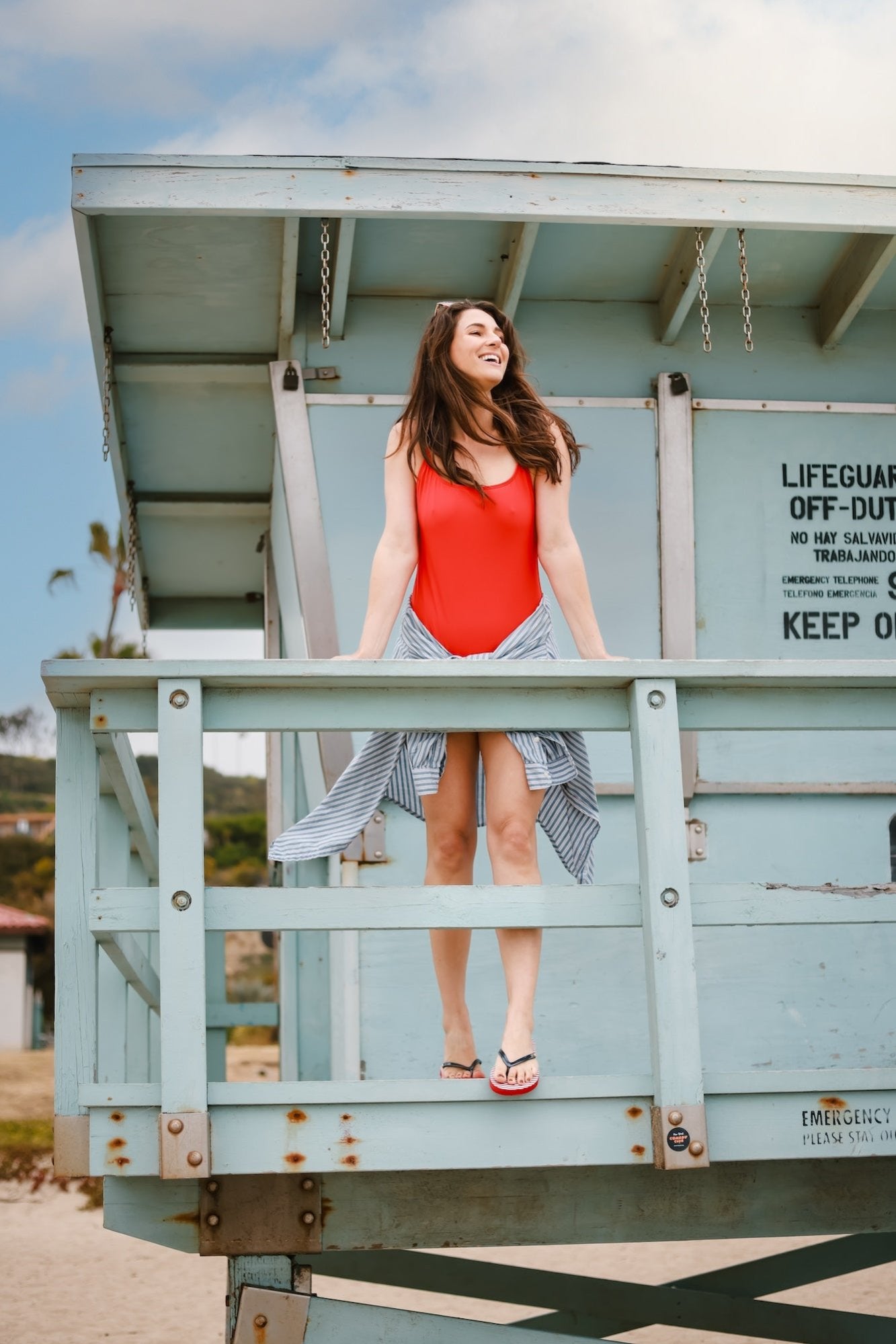 Woman sitting on a blue Lifeguard post at the beach leaning over the railing wearing Harmony 783 red white and blue grounding plug flip flops
