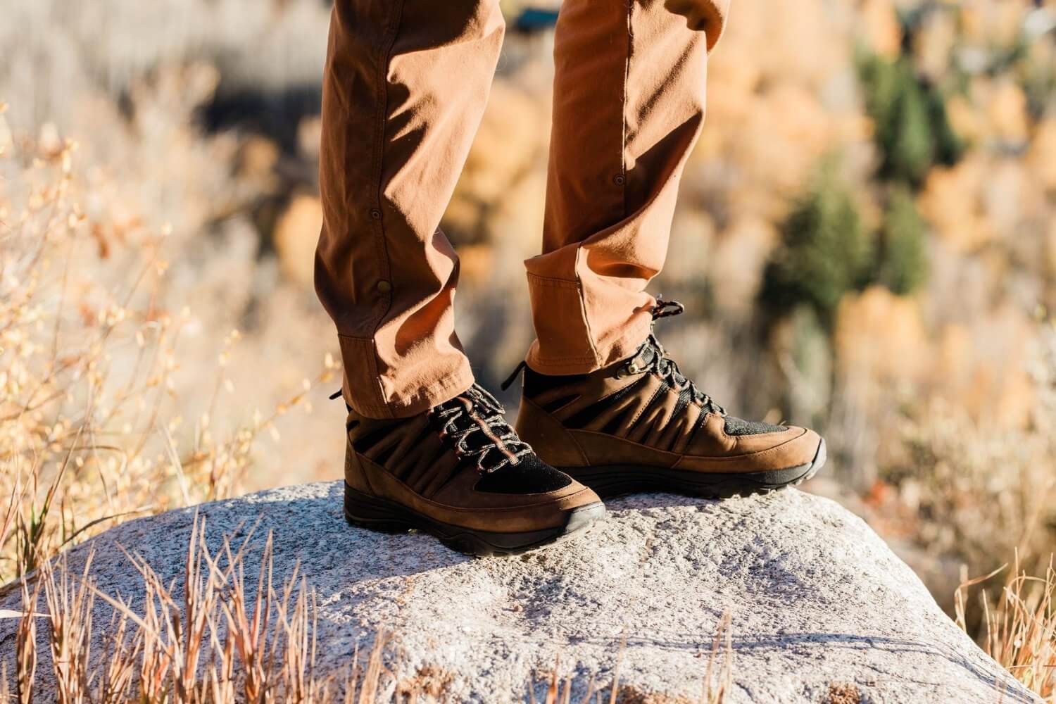 Man Standing on rock while hiking in grounding high top trail shoes brown leather and black mesh