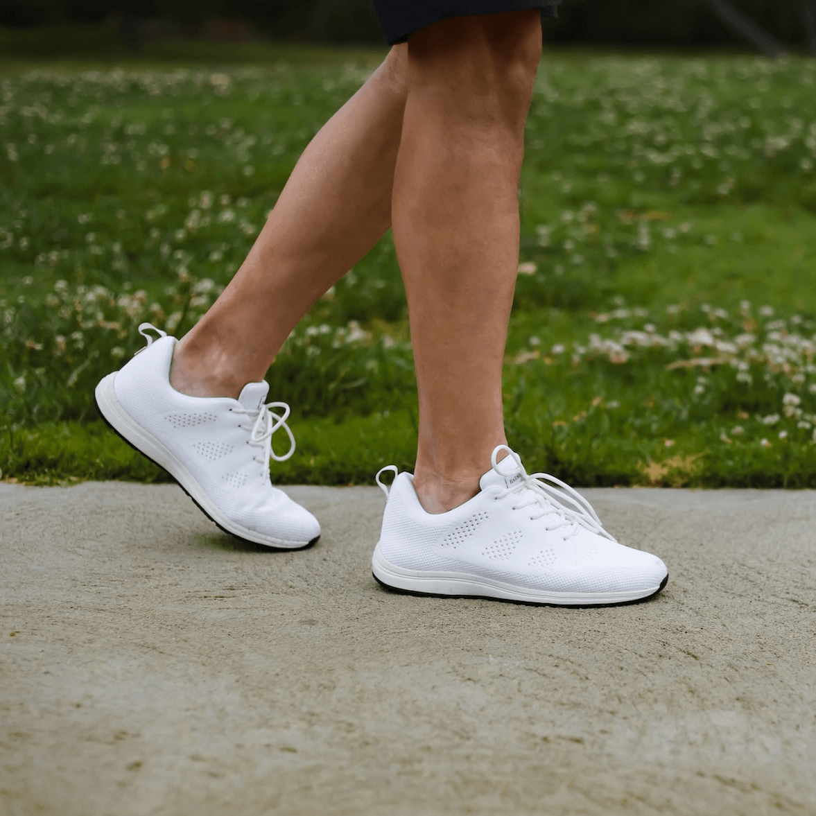 Walking in park wearing white lace-up tennis shoes recycled plastic for grounding