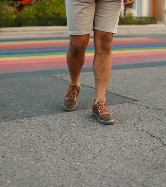 Man walking across the street wearing shorts and brown leather grounding walking shoes with grey soles