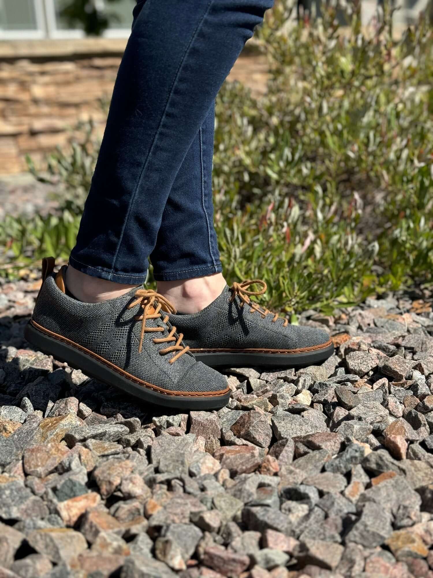 woman walking from left to right on stone pebbles wearing grounded knit walkers in charcoal and cognac