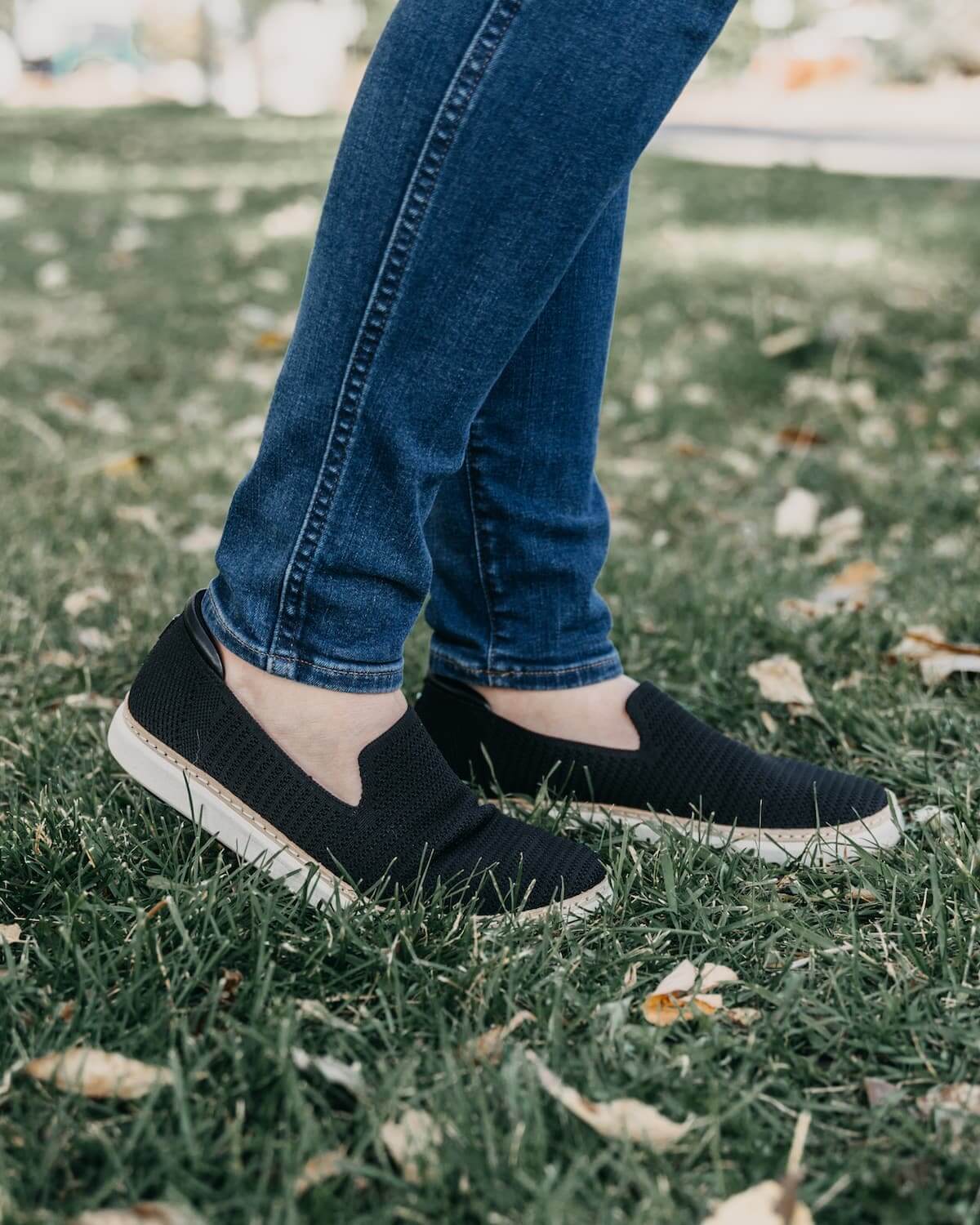 Woman wearing jeans and black and white bamboo grounding slip-ons for earthing on grass