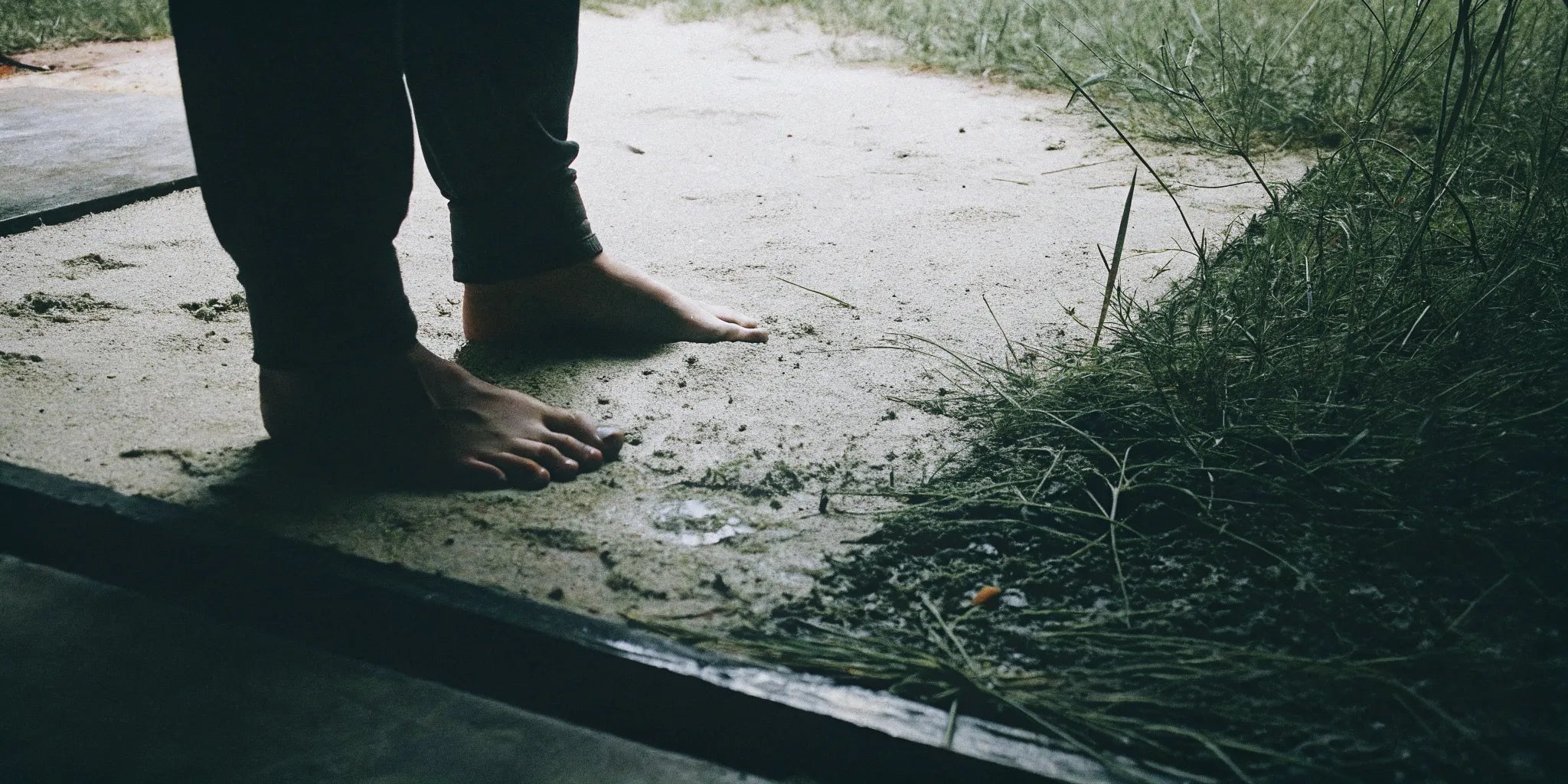 A close-up of feet on grass, sand, and concrete surfaces for grounding.