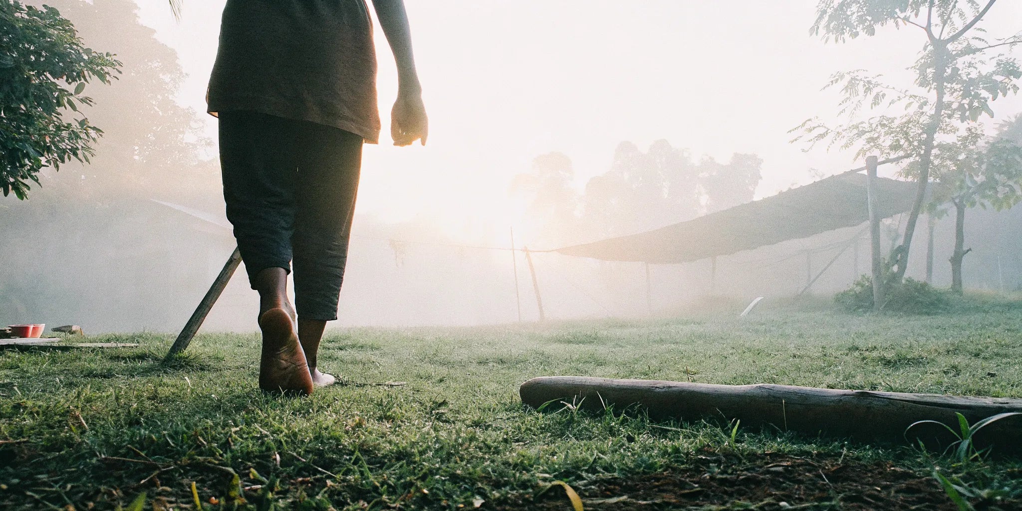 A person walking barefoot on dew-covered grass during a calm sunrise, reconnecting with the earth