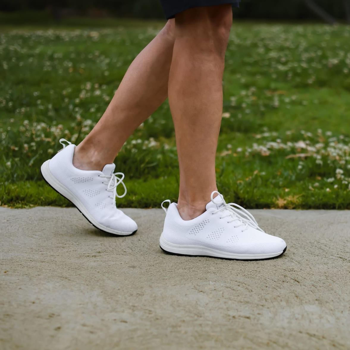 Walking in park wearing white lace-up tennis shoes recycled plastic waterproof for grounding