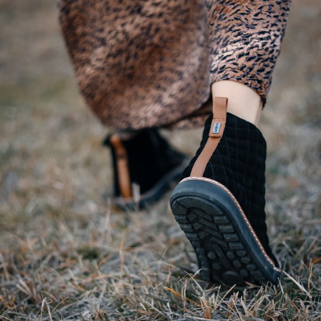 Woman walking away showing the cognac trim and sole of the black quilted grounding high-top