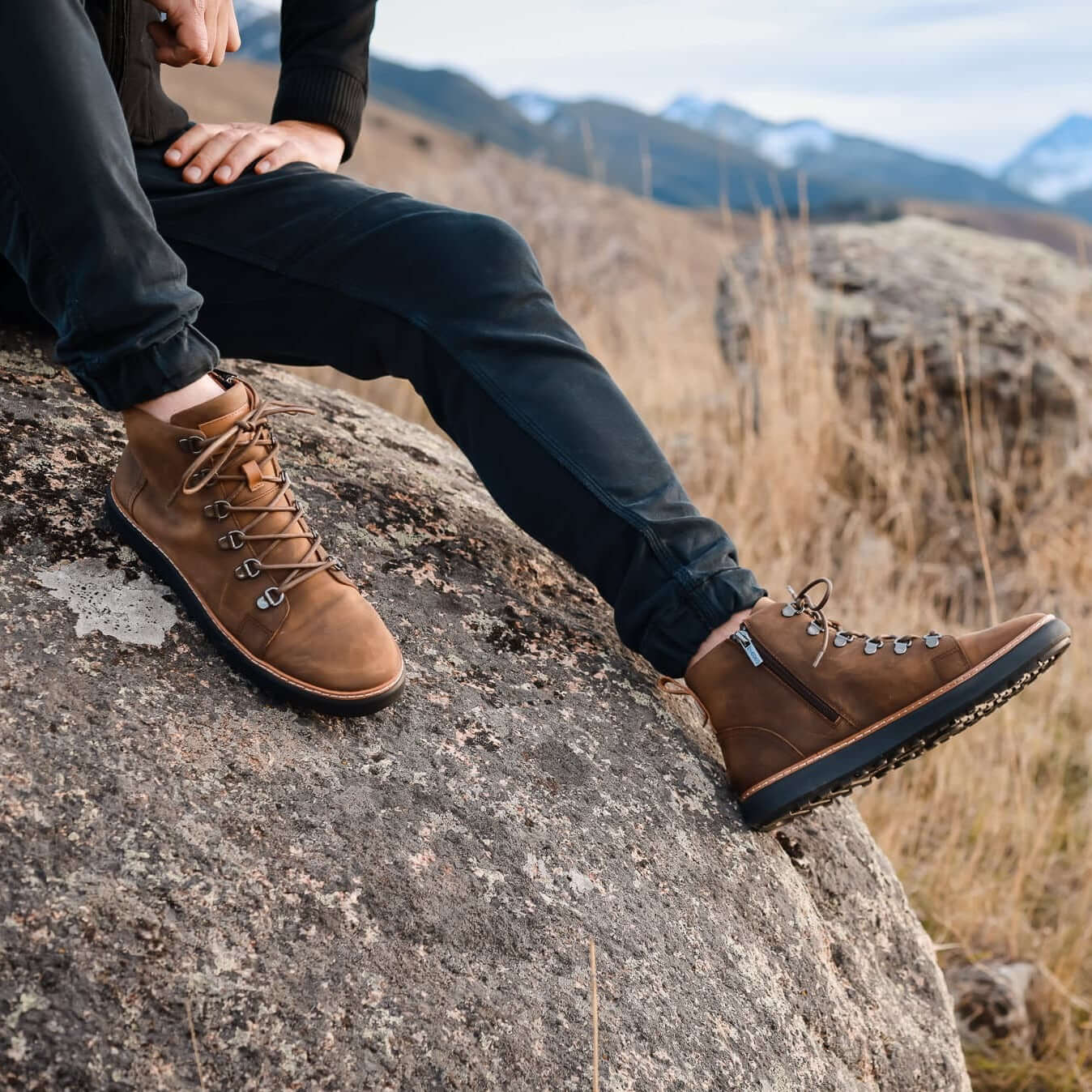 Man wearing high top brown leather zip up grounding boots on rock in winter