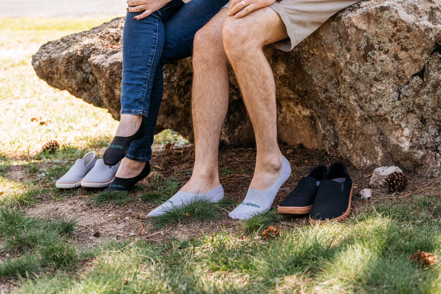 Man and woman sitting on rock wearing earthing/grounding socks with feet in the grass