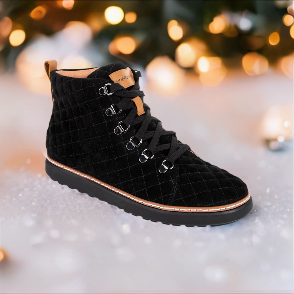 Black quilted high top grounding boot sitting on snow with string lights in background