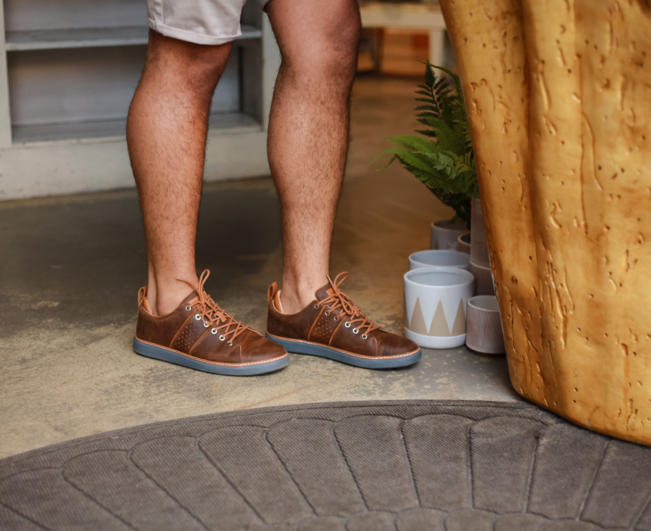 Man wearing brown leather grounding walkers with grey soles next to flower pots