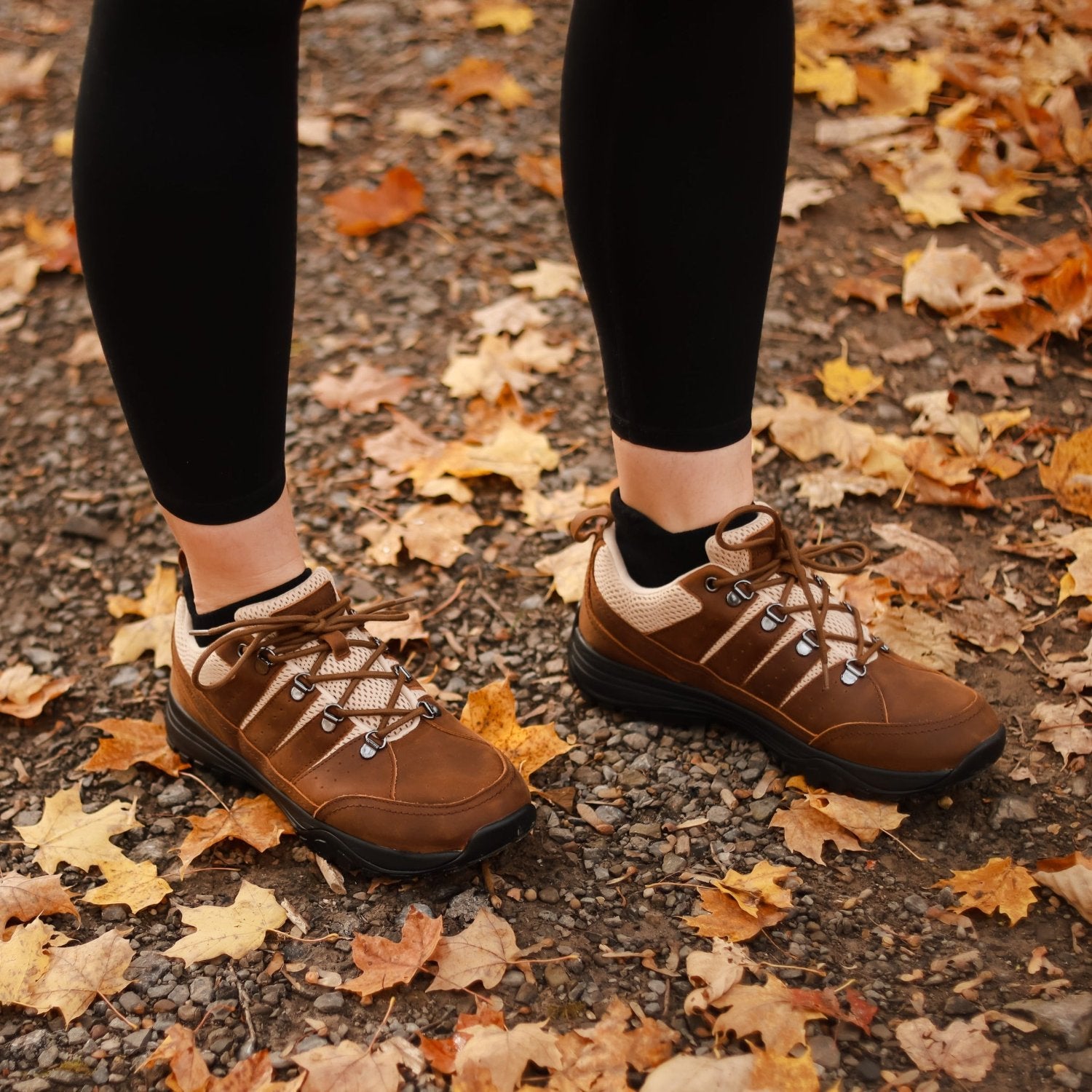 Woman wearing black leggings and brown leather grounding trail shoes in fall leaves