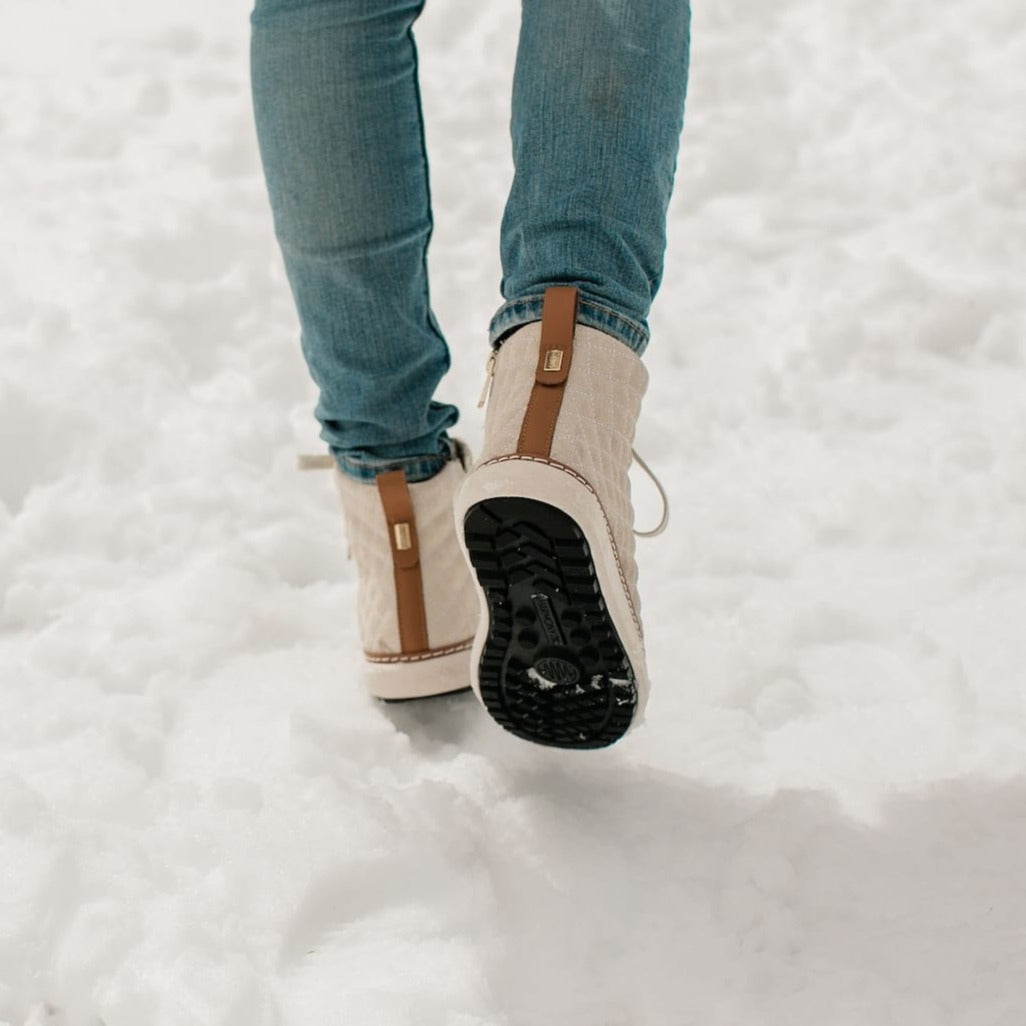 Woman walking showing the tread of the gold creme quilted high top for grounding in snow.