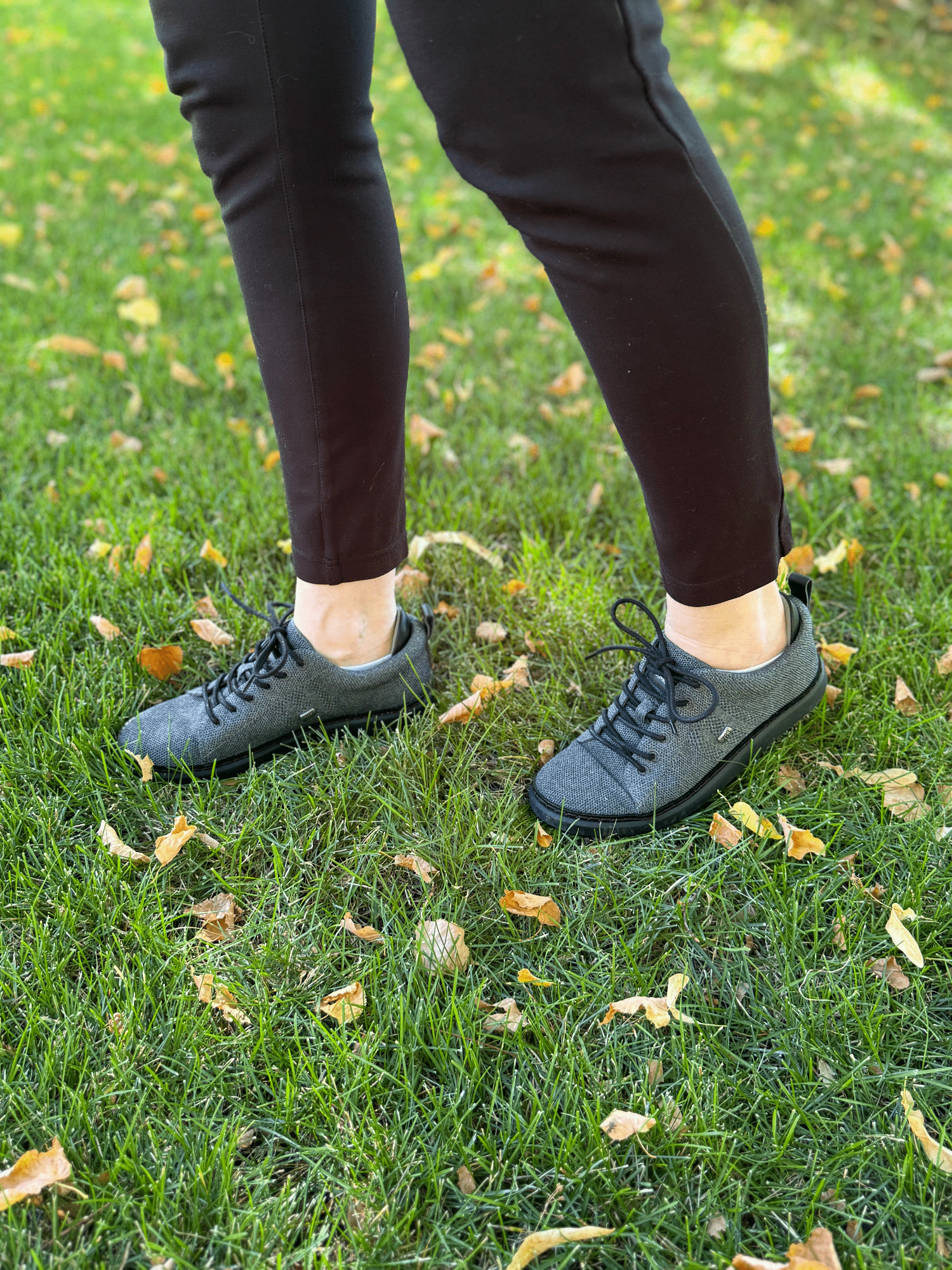 woman walking on grass with leaves wearing grounding knit walkers in charcoal and black