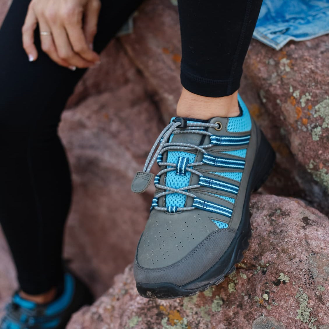 Woman wearing Taylor Trail Shoe in Grey Nubuck with Blue Mesh on Rocks