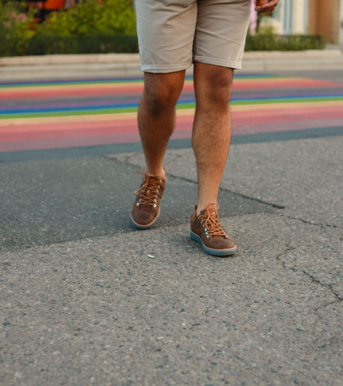 Man walking across the street wearing shorts and brown leather grounding walking shoes with grey soles