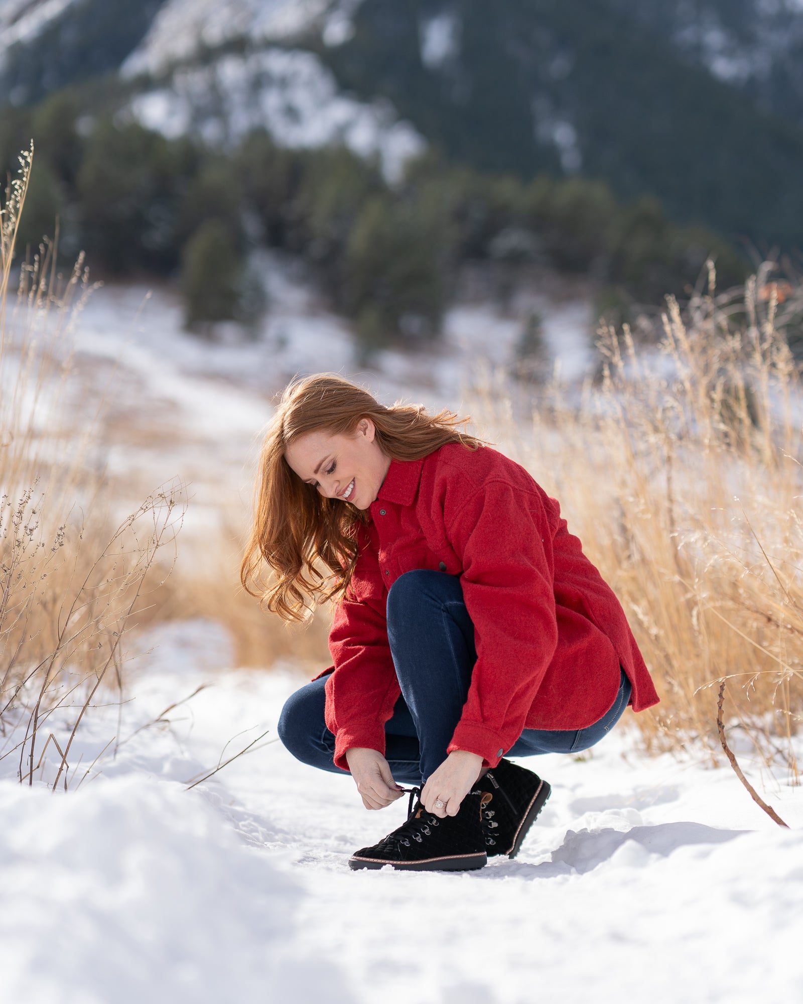 Woman kneeling down in snow to tie shoelace for black quilted grounding high-top