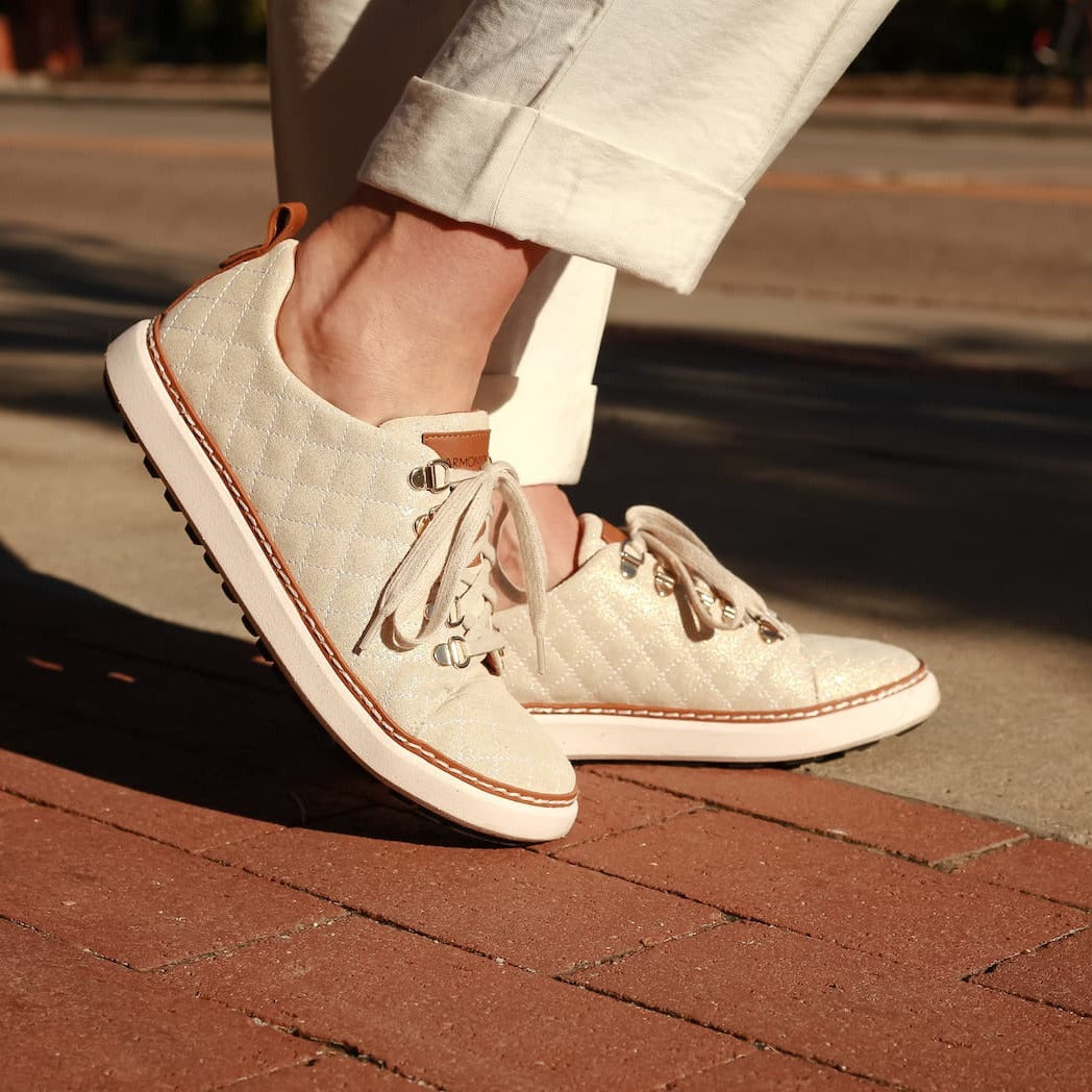 Woman wearing Gold Creme Quilted Sparkly Grounding walking shoe on brick