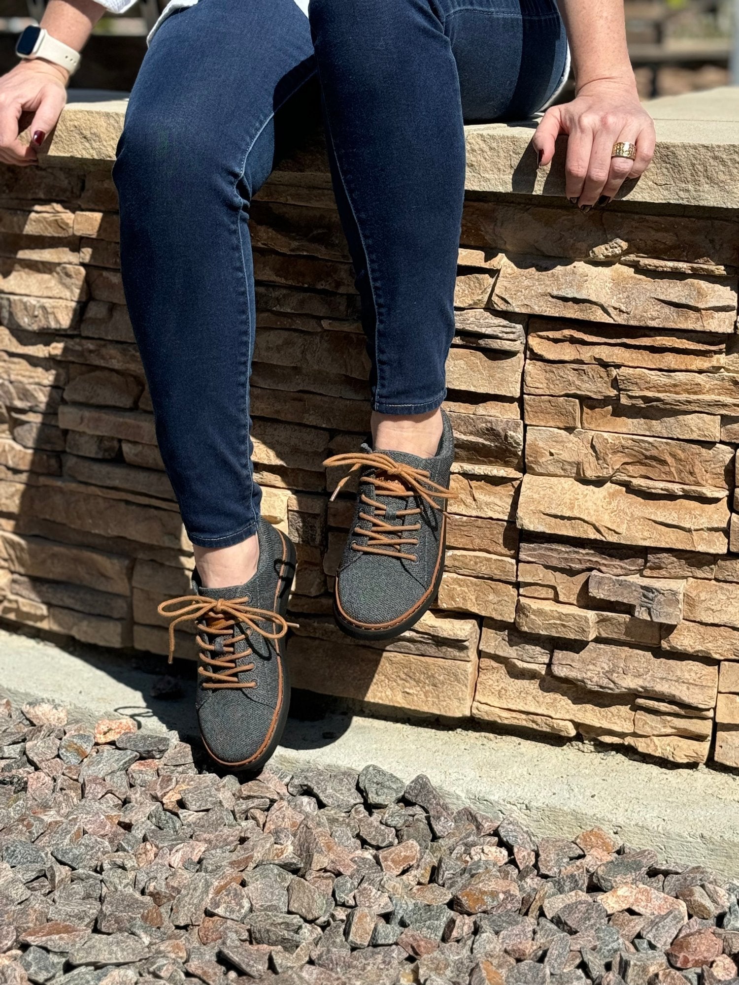 woman sitting on rock near pebbles with legs hanging off ledge wearing emerson knit grounding walkers in charcoal and cognac