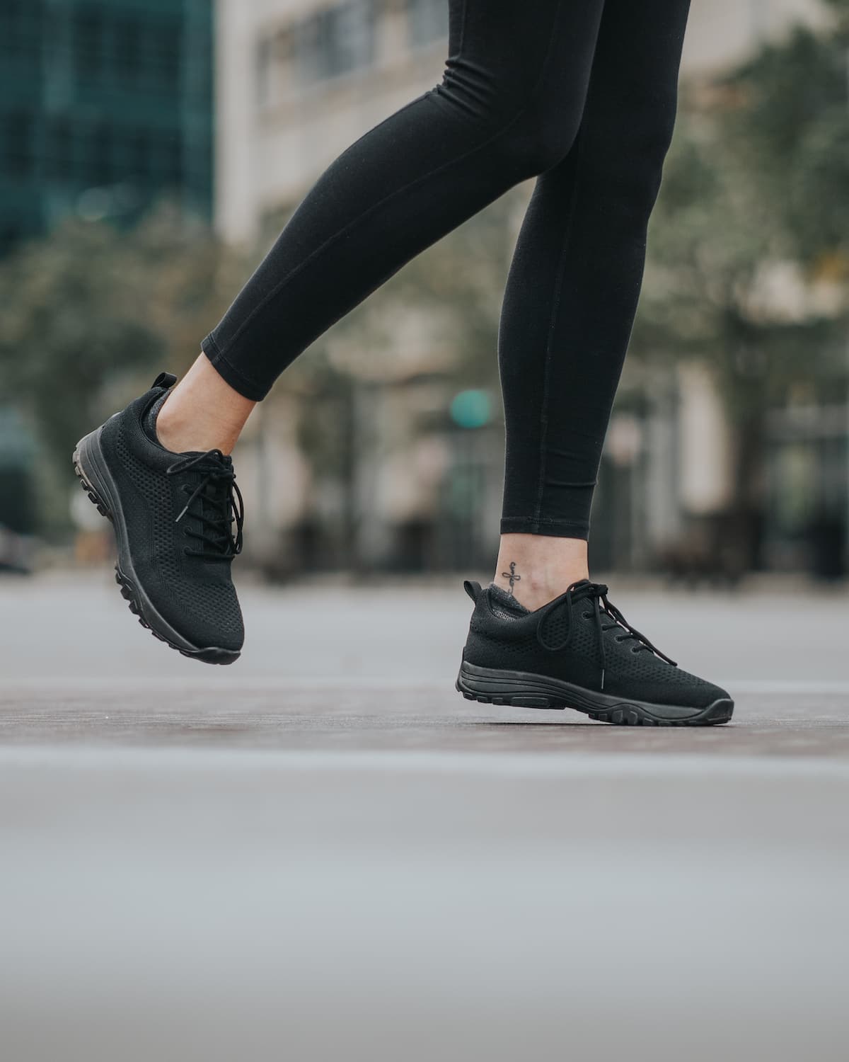 Lifestyle photo of woman wearing black leggings and black bamboo knit grounding sneakers with city in background