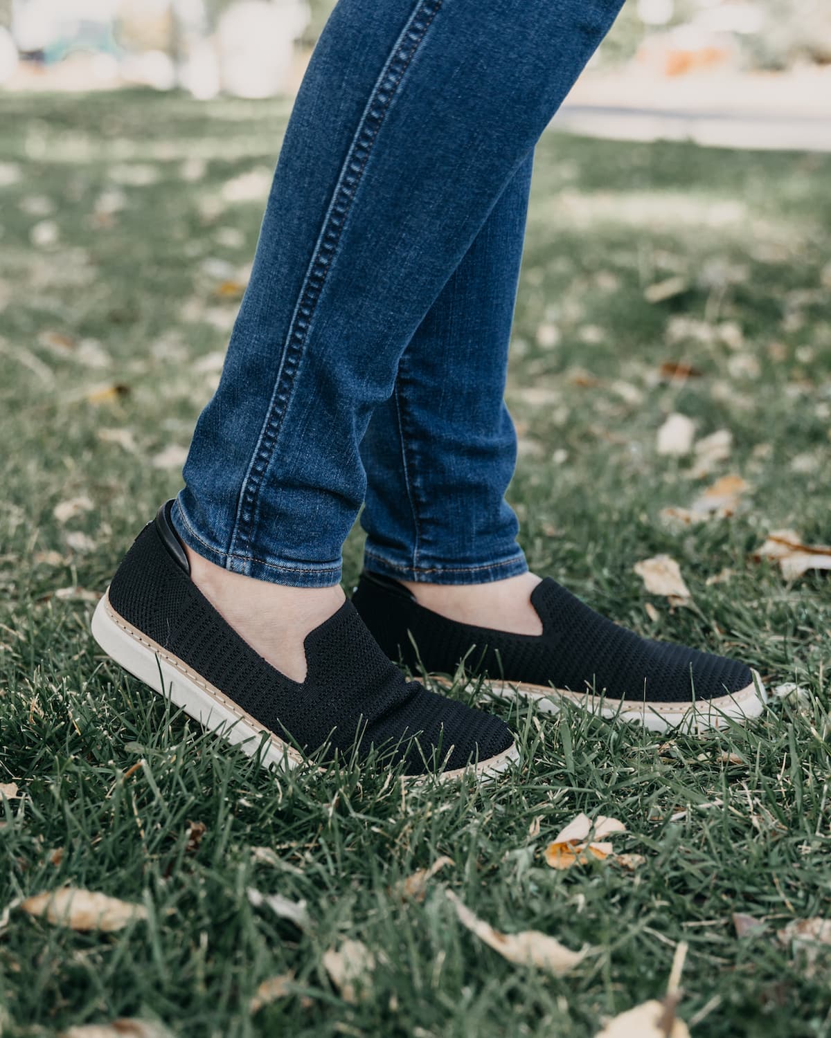 Woman wearing jeans and black and white bamboo grounding slip-ons for earthing on grass