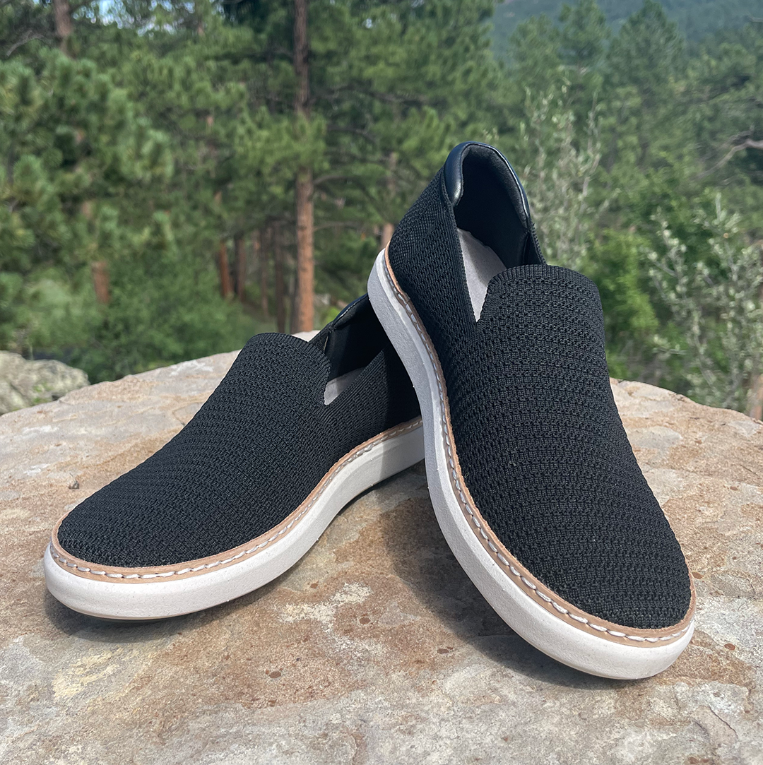 Stacked view of black and white bamboo grounding knit slip-ons on stone