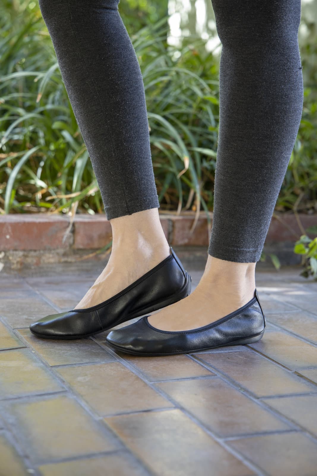 Woman wearing leggings and black leather grounding ballet flats on brick