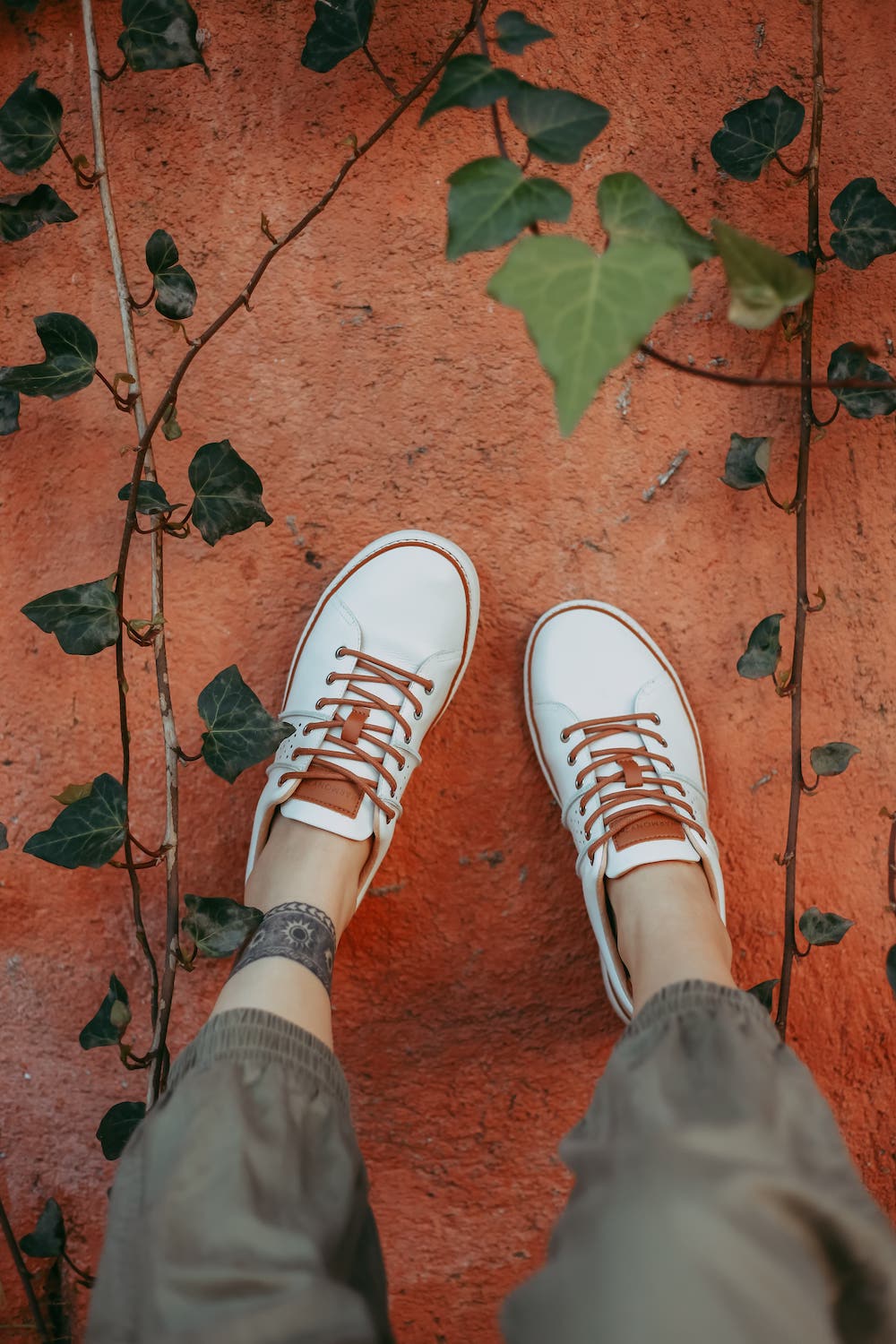 Woman wearing green pants and white leather grounding walking shoes on concrete wall with vines