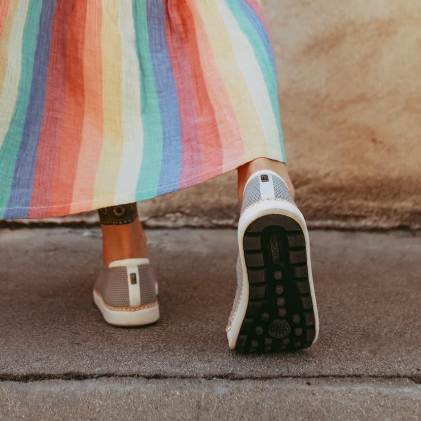 Woman wearing colorful skirt and grey bamboo knit grounding slip-on walking away from camera