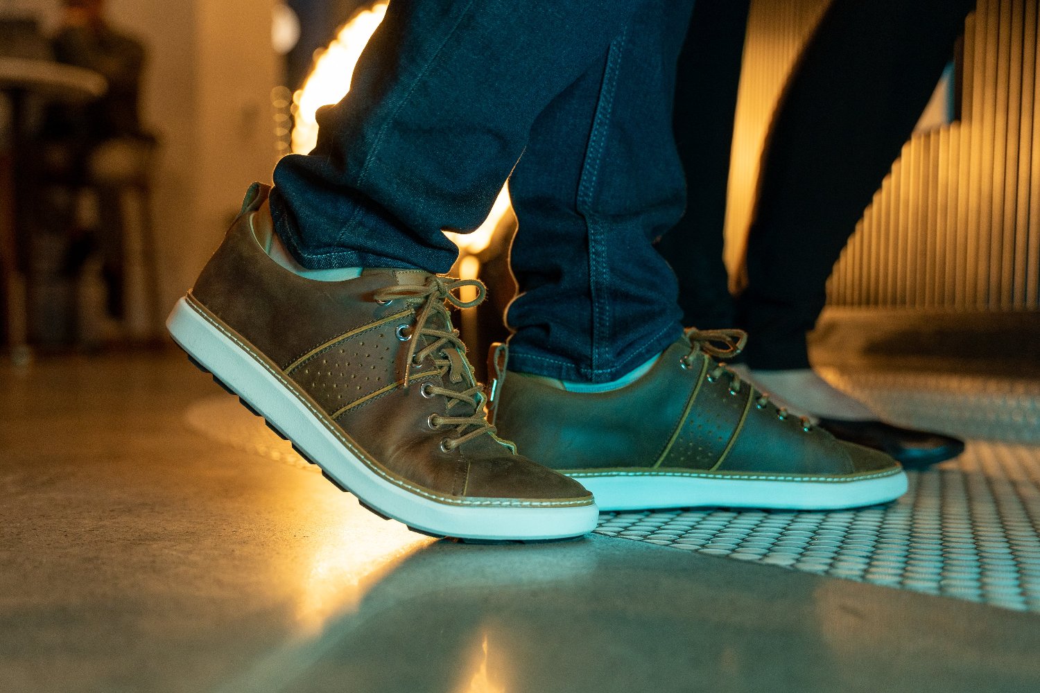 Man wearing brown leather walking shoes with jeans on concrete inside