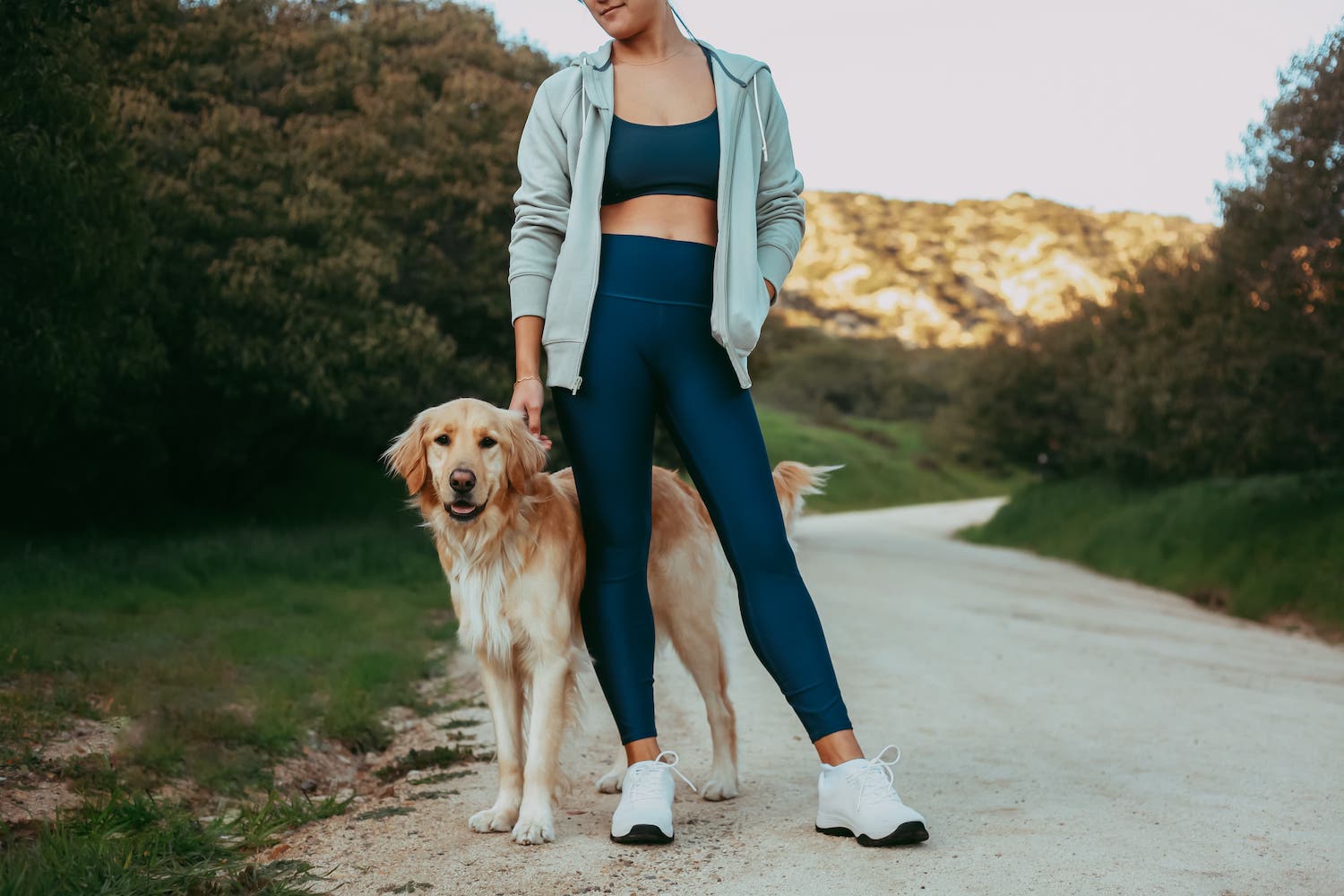 Woman walking dog in park wearing blue leggings and white bamboo grounding sneakers